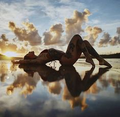 a woman is laying on the beach at sunset