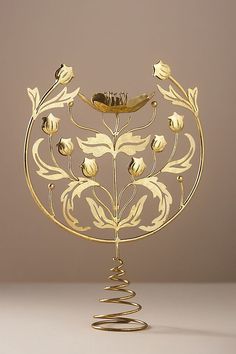 a golden metal sculpture with flowers and leaves on it's sides, in front of a beige background