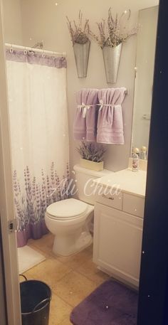 a white toilet sitting in a bathroom next to a sink and shower curtain with lavender flowers on it