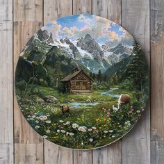 a plate with a painting of animals in the grass and mountains behind it on a wooden wall