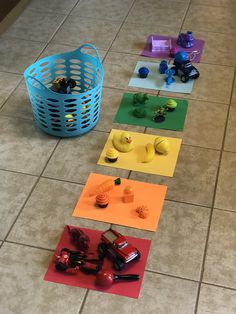 some toys are laying out on the floor in front of a blue basket and two red cars