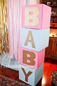 a pink and blue block with gold glitter letters on it that spell out the word baby