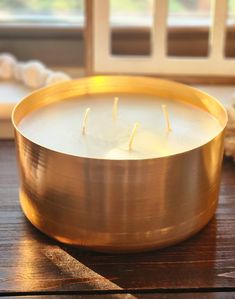 a candle is sitting in a metal bowl on a wooden table next to a window