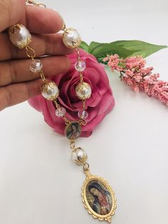 a hand holding a necklace with an image on it and pearls hanging from the chain