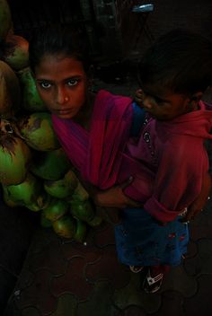 a woman carrying a child on her back next to a bunch of green coconuts