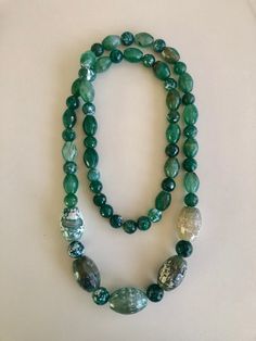 "Unique and bold, this continuous necklace of dyed fire and snakeskin agate with chalcedony mixed in features several hues of green.  Faceted oval and round crackle-look beads run the length on both sides of this 36\" piece, while the necklace center is comprised of larger 30mm faceted agate ovals in differing shades.  Most of these unusual beads are about 12-10mm in size and with approximately 58 beads around the strand, it weighs in at about 9oz.  In beautiful condition and poised to liven up Luxury Green Agate Beaded Necklace, Luxury Green Agate Beaded Necklaces, Snakeskin Agate, Fire Agate, Faceted Bead, Snake Skin, Agate, Beaded Necklace, Jewelry Necklaces