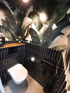 a bathroom with black and white tiled walls, toilet and plant mural on the wall