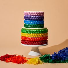 a multicolored cake on a white pedestal surrounded by confetti