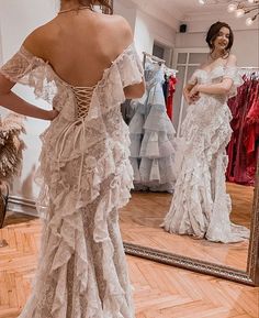 a woman is looking at herself in the mirror while wearing a wedding dress with ruffles on it