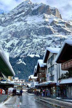 people are walking down the street in front of snow covered mountains and buildings with shops on each side