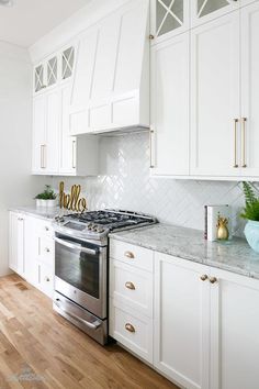 a kitchen with white cabinets and marble counter tops, gold accents on the oven hood