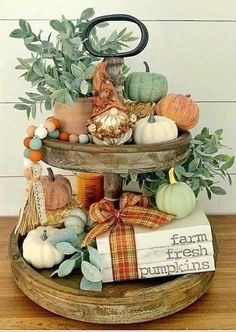 a three tiered tray with pumpkins and gourds on it, sitting on top of a wooden table