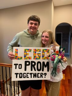 two people standing next to each other holding a sign that says yes to prom together