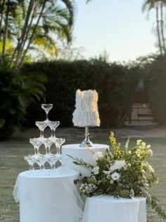 two white candles are sitting on top of each other in front of some flowers and greenery