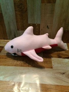 a pink stuffed shark laying on top of a wooden floor