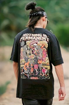 a man walking down a dirt road while wearing a black shirt with an image on it