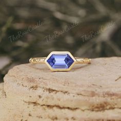 a gold ring with an oval cut blue sapphire gemstone in the center, sitting on top of a rock