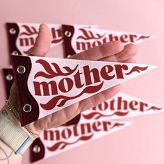 a hand holding a sticker with the word mother written on it in red and white