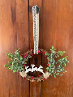 a wreath with deers and holly on it hanging from a wooden door, next to a pair of scissors