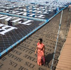 a woman walking on the side of a road next to a soccer field covered in blue and white letters