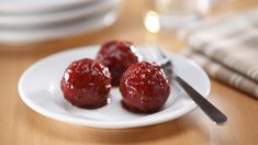 three cherries on a white plate with a fork