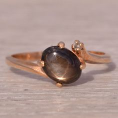 This Stunning Piece, Known As The Starry Night, Features A Captivating Oval Cabochon Black Star Sapphire With A Charming Star That Floats Across The Top. The Star Sapphire Is Elegantly Set In 14 Karat Rose Gold, Complemented By A Single Sparkling Diamond Accent. The Ring Is Currently A Finger Size 6 But Can Be Adjusted To Any Finger Size For An Additional Charge Upon Request, Ensuring A Perfect Fit. Black Star Sapphire, Black Star Sapphire Ring, Star Sapphire Ring, Star Sapphire, Black Star, Rose Gold Color, Oval Cabochon, Sparkle Diamonds, Black N Yellow