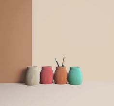 three different colored vases sitting next to each other on a white table with a beige wall in the background