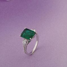 an emerald and diamond ring on a purple background