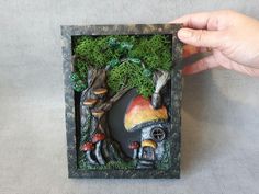 a hand holding up a small box with a mushroom house and mushrooms in the woods