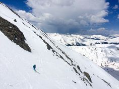 a person skiing down the side of a snow covered mountain with mountains in the background