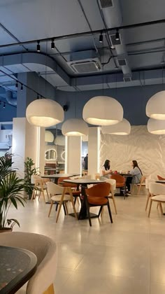 people are sitting at tables in the middle of a room with round lights hanging from the ceiling