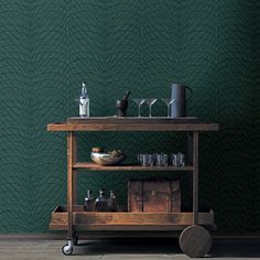 a bar cart with bottles and glasses on it in front of a green wallpaper