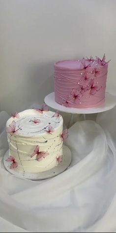 two cakes with pink frosting and flowers on them sitting on top of a white table cloth