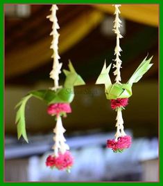 three paper cranes hanging from strings with flowers in the foreground and a green frame around them