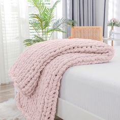 a pink blanket on top of a bed next to a chair and potted plant