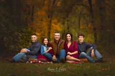 a family posing for a photo in front of trees with fall leaves on the ground