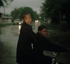 two young men riding on the back of a motorcycle down a street at night time