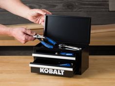 a person is holding scissors and pliers in a tool box on top of a table