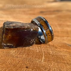 two wedding bands with wood inlays are sitting on top of a piece of wood