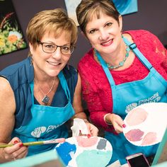 two women in aprons are painting with paintbrushes