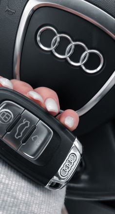 a hand holding a car key in front of an audi logo on the steering wheel