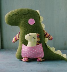 a green stuffed animal with a pink and white polka dot dress sitting on the ground