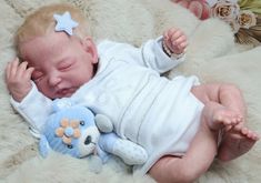 a baby laying on top of a white blanket next to a stuffed animal toy with its eyes closed