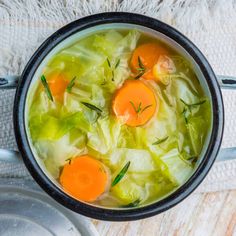 a pot filled with cabbage and carrots on top of a white cloth next to spoons