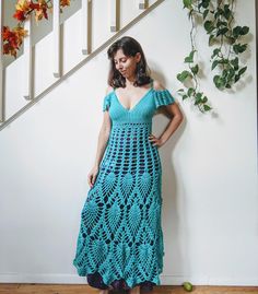 a woman in a blue crochet dress standing next to a stair case and plant