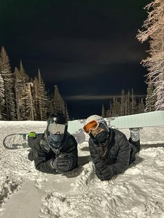 two snowboarders sitting in the snow with their skis and goggles on