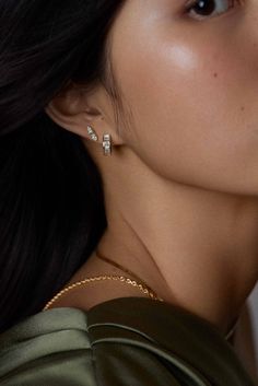 a woman with long black hair wearing gold and diamond earrings on her neck, looking off to the side