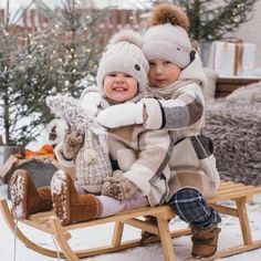 two young children sitting on a sled in the snow, one holding onto the other