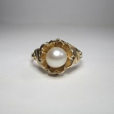 A pretty flower ring with a natural pearl set in the center. Ring size 6 1/4. Pearl measures about 6.25mm x 6.4mm. Ring Top Dimensions: 11.5mm x 10.4mm (0.45" x 0.41") Ring Top Height: 7mm (0.27") Band Width: 2mm Markings: "10k" Weight: 2.75 grams This is an estate piece in excellent condition. It has been professionally cleaned and sanitized for your peace of mind. The Trading Post is based in Chardon, Ohio. We carry a large selection of gold and silver jewelry, bullion, numismatic coins, and m Classic Round Flower Ring In 14k Gold, Classic 14k Gold Round Flower Ring, Classic Wedding Rings With Flower Shape, Classic 14k Gold Flower Ring, Classic Yellow Gold Round Flower Ring, Classic Yellow Gold Flower Ring, Classic 14k Gold Flower Ring For Anniversary, Classic 14k Gold Flower Ring For Formal Occasions, Classic Formal Rings With Flower Shape