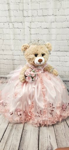 a teddy bear in a pink dress sitting on a wooden floor next to a brick wall